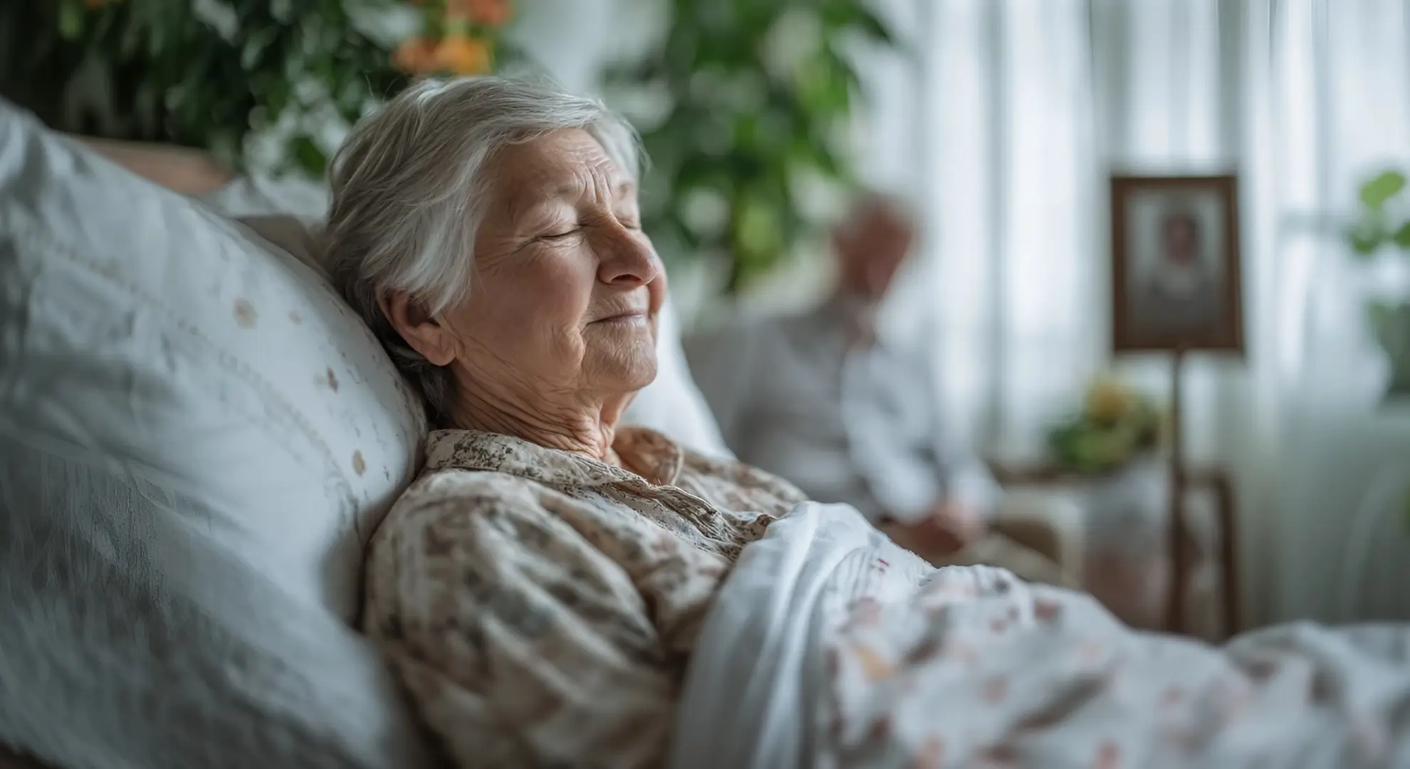 An elderly woman with gray hair lies in bed with a serene smile on her face.